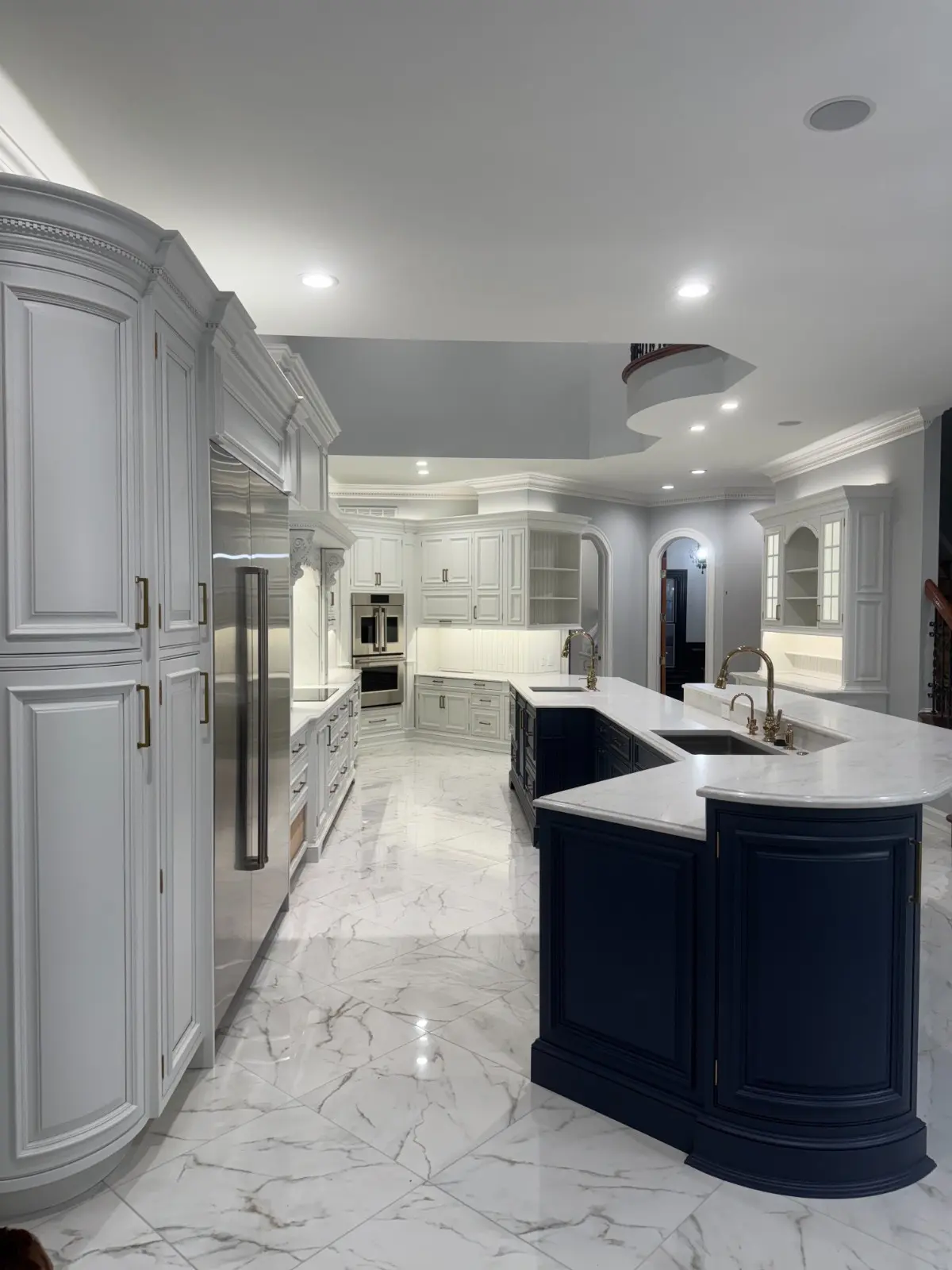 Luxurious kitchen featuring Martzall's Custom Surfaces white marble flooring and matching countertops paired with elegant navy blue and white cabinetry.