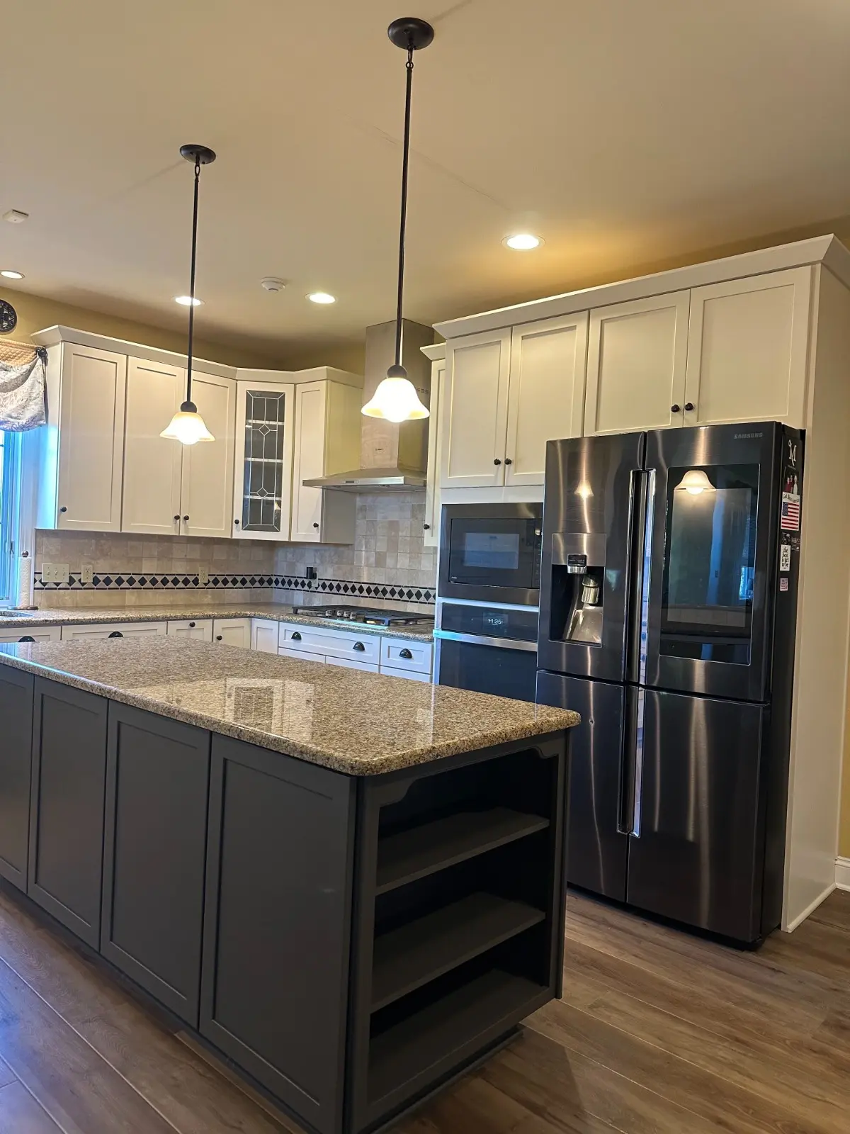 Classic kitchen remodel featuring Martzall's Custom Surfaces polished granite countertops paired with a dark grey island, white cabinetry, and earth-toned backsplash.