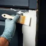 A professional painter applies a smooth white finish to dark cabinets, demonstrating the high-quality results of cabinet refacing in Lancaster County, PA.