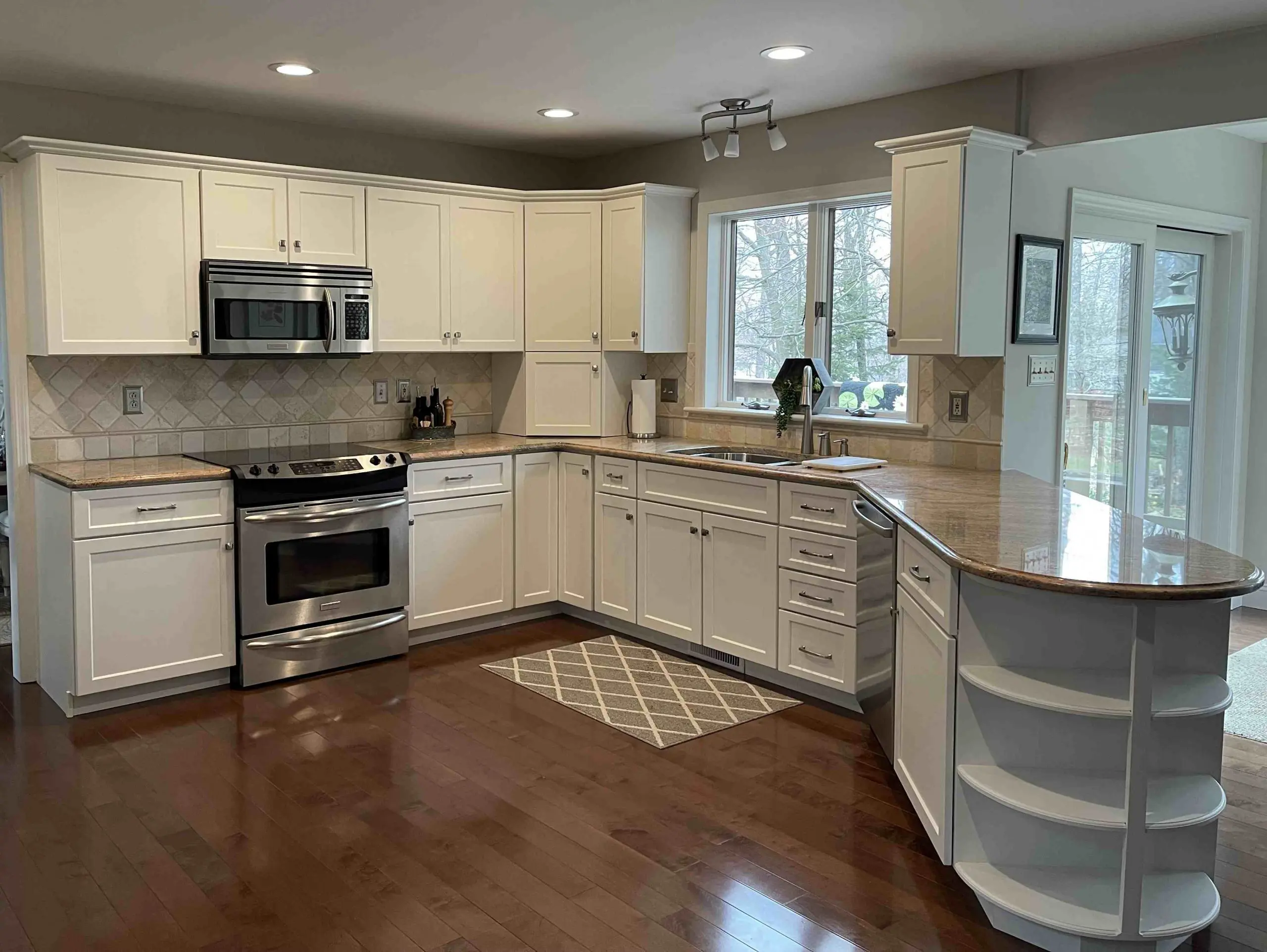 A bright, modern kitchen by Penguin Clean Co featuring white cabinets, stainless steel appliances, and polished granite countertops on a dark hardwood floor.