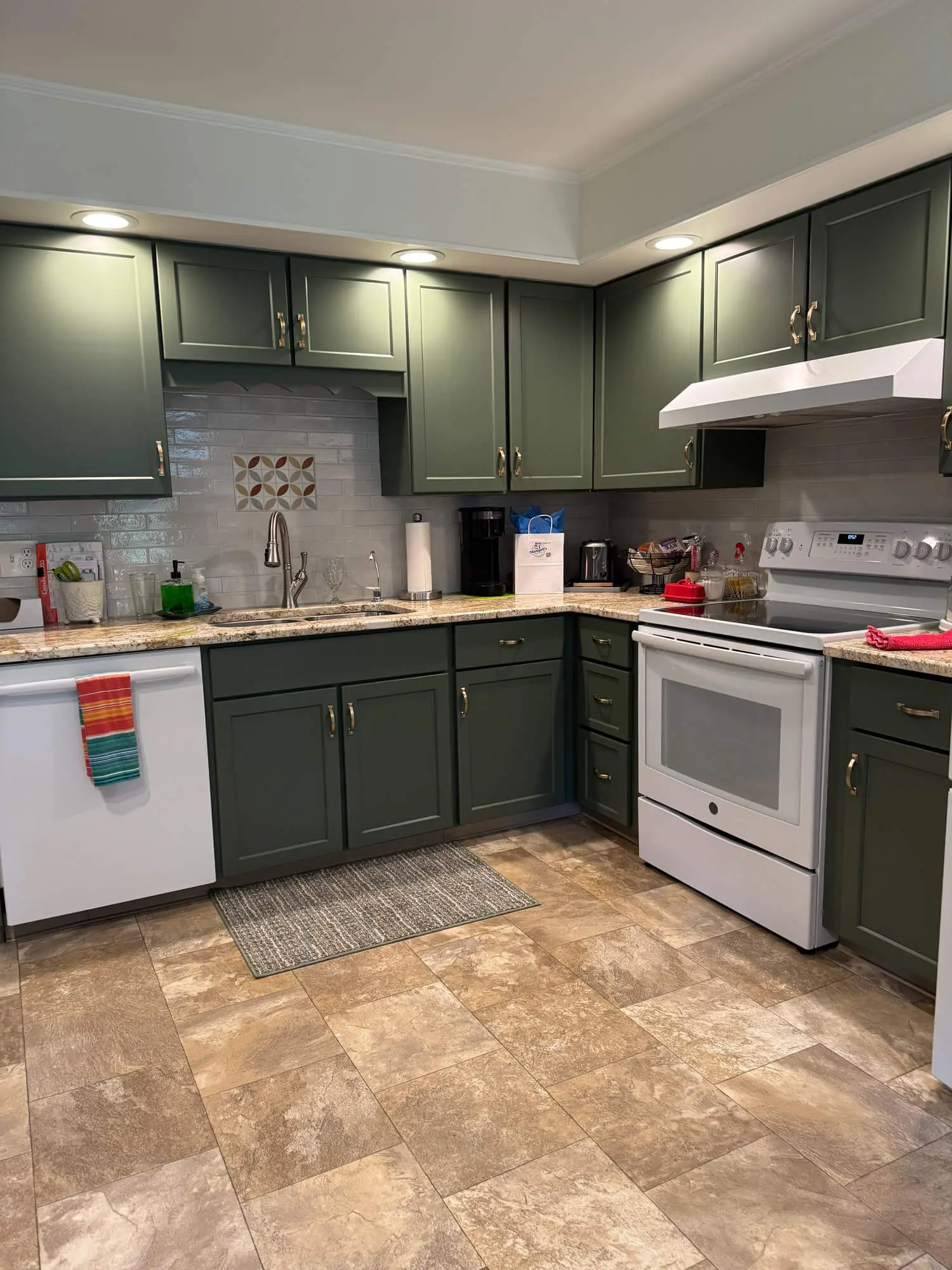 Modern kitchen with deep green painted cabinets, white appliances, subway tile backsplash, and warm recessed lighting creating a clean and refreshed space
