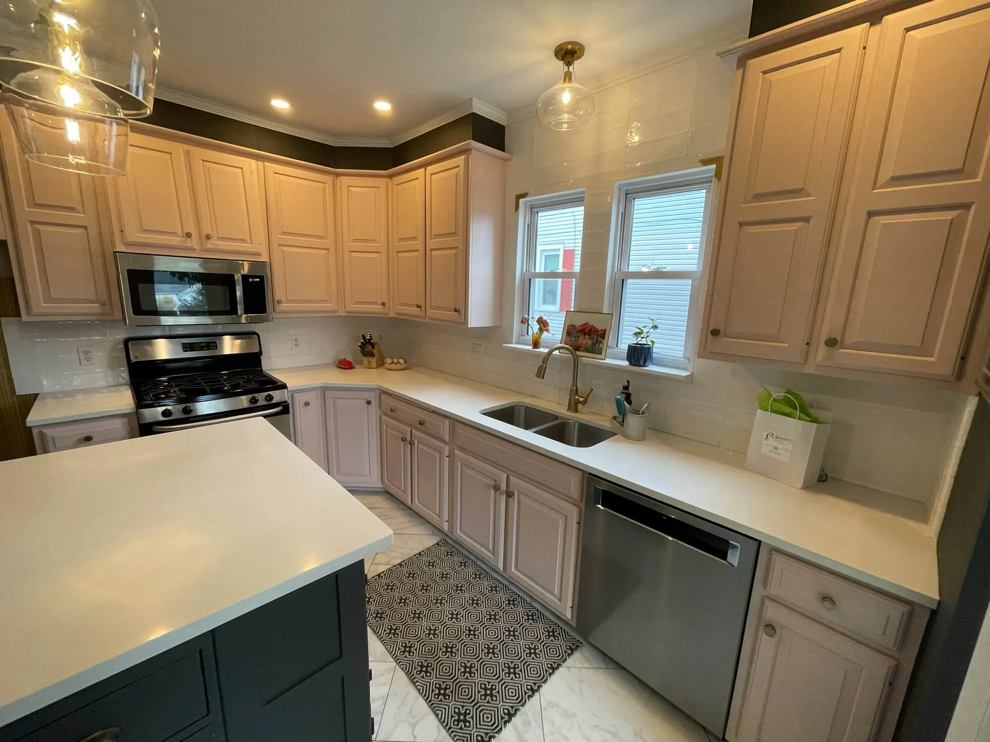 Bright kitchen featuring freshly painted light beige cabinets, white quartz countertops, stainless steel appliances, subway tile backsplash, and a contrasting dark island for a clean, modern look