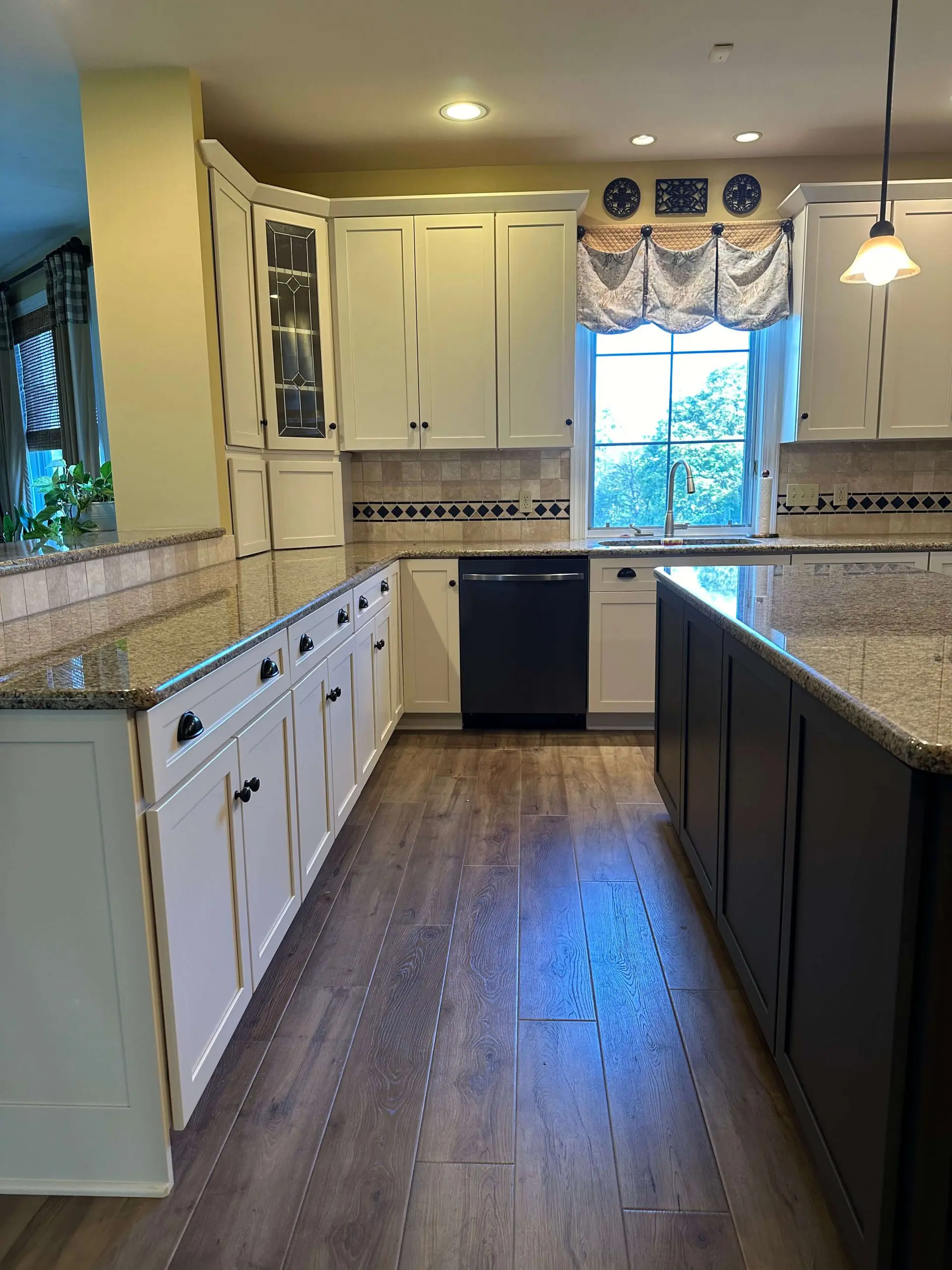 Elegant kitchen remodel by Martzall's Custom Surfaces showcasing cream shaker cabinets, granite countertops, and a dark charcoal island against hardwood flooring.