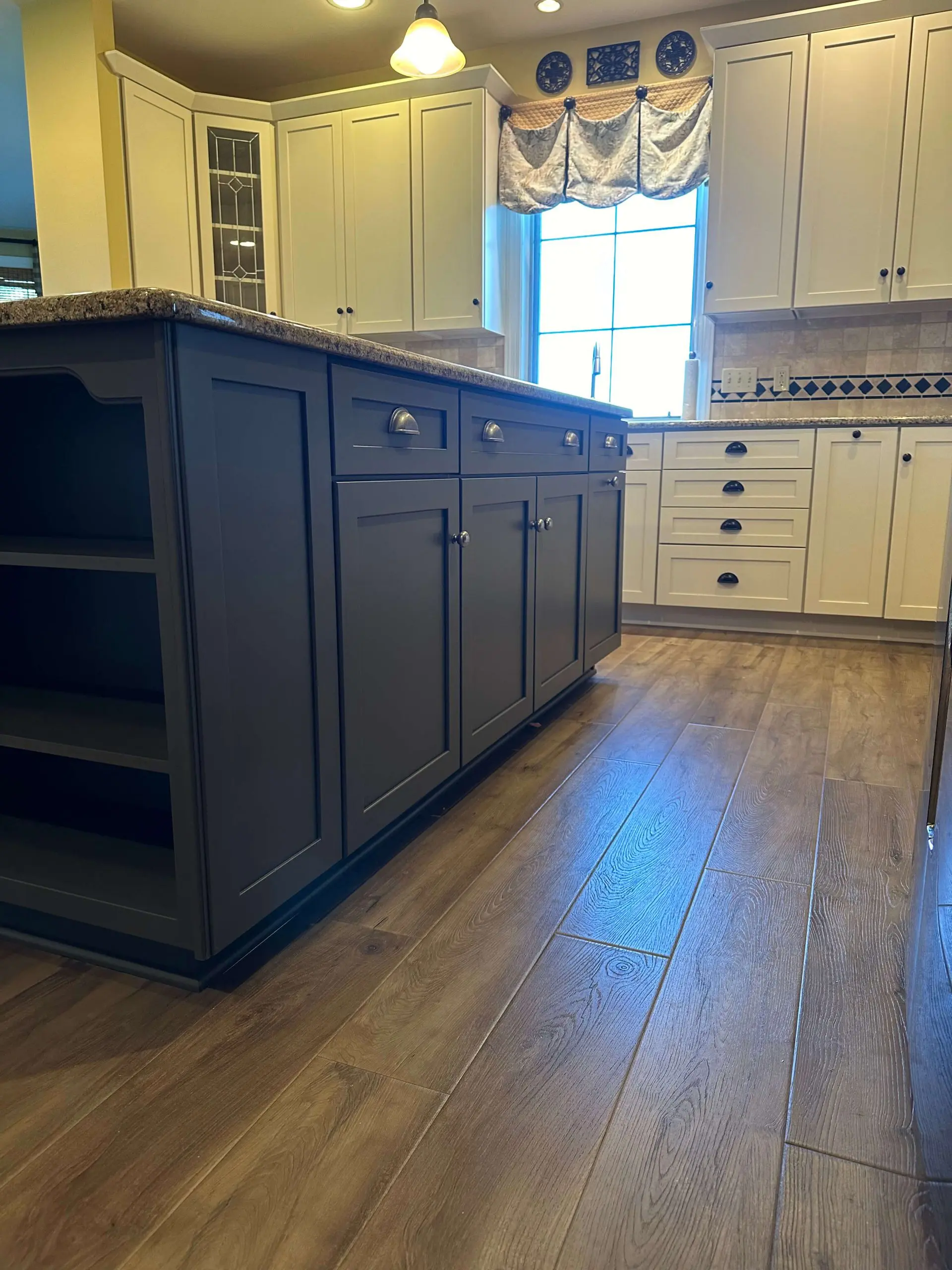 Modern kitchen renovation featuring charcoal grey island cabinetry and light wood plank flooring by Martzall's Custom Surfaces.
