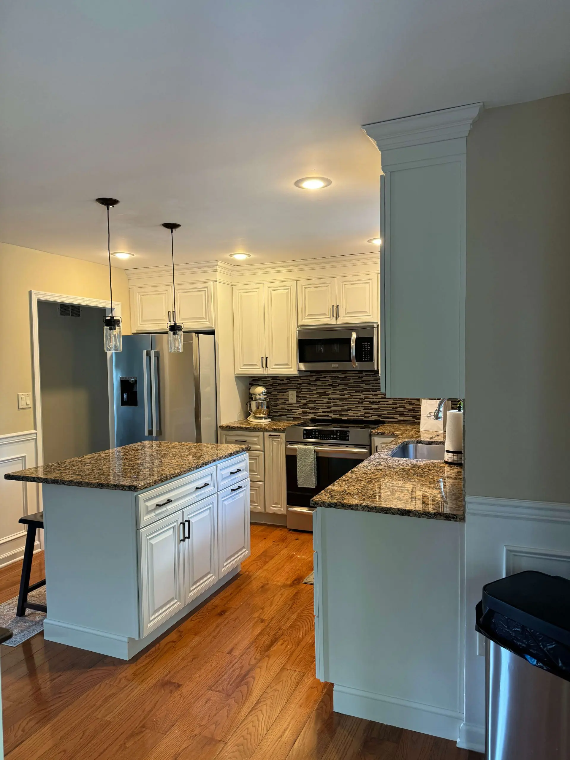Martzall's Custom Surfaces showcases a modern kitchen renovation featuring elegant granite countertops, white raised-panel cabinetry, and a matching center island on polished hardwood flooring.