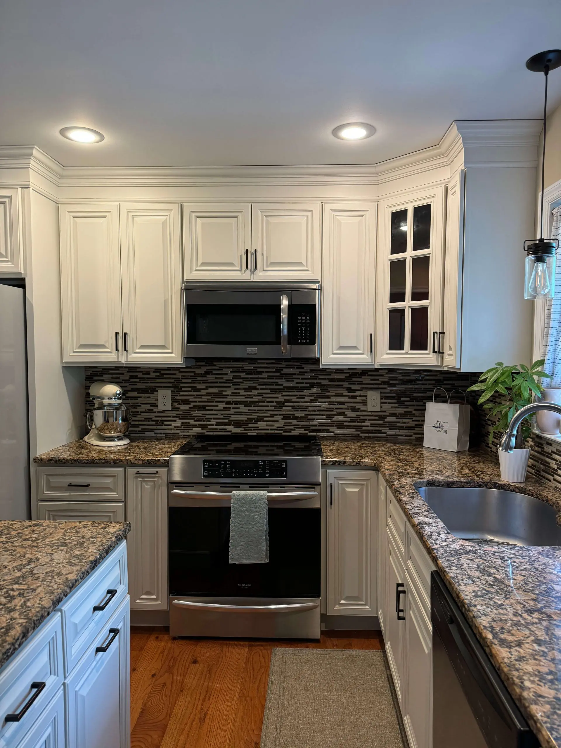 Modern kitchen renovation by Martzall's Custom Surfaces featuring cream-colored cabinetry, earthy granite countertops, and a linear mosaic tile backsplash.