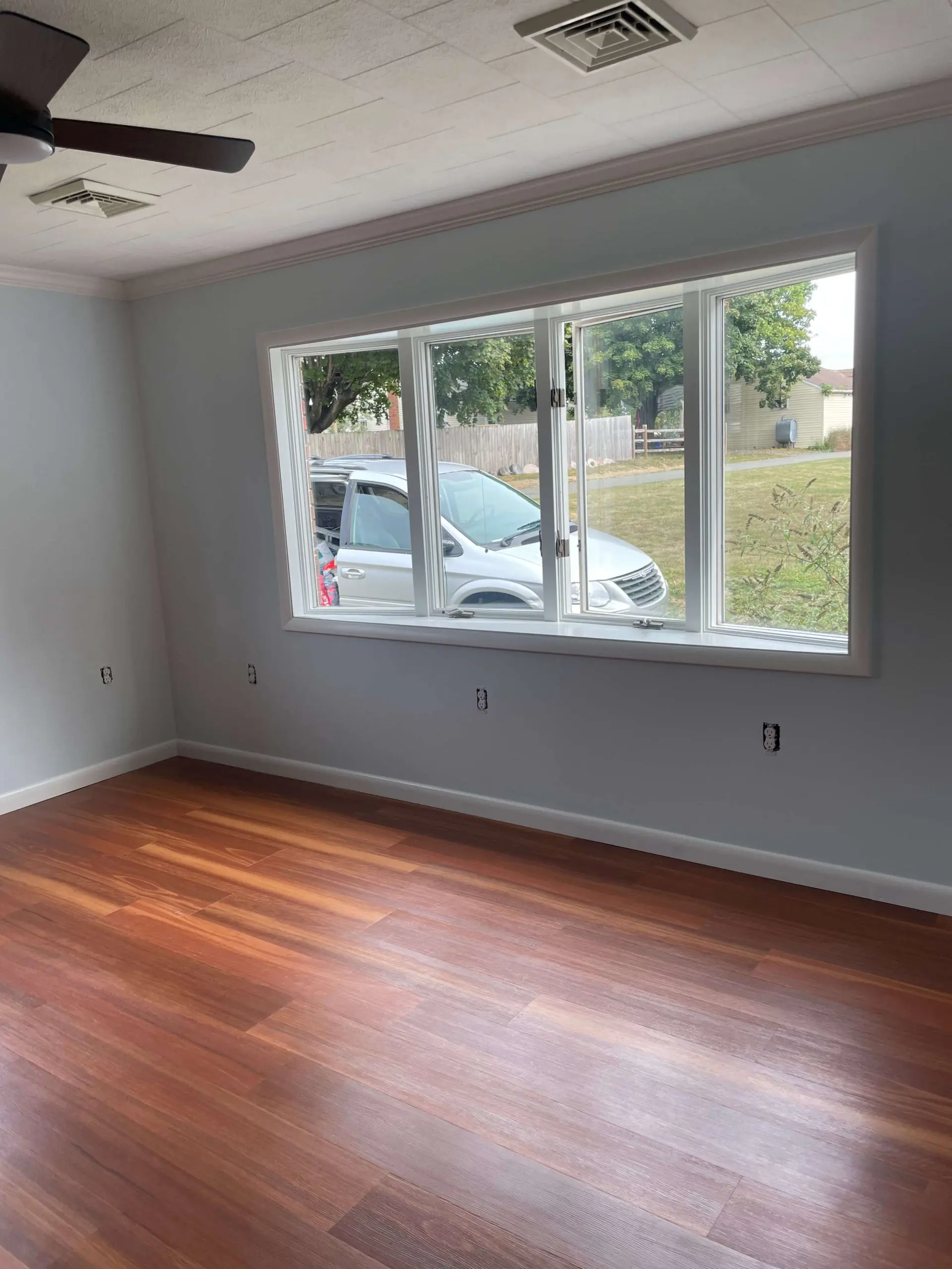 Living room renovation showcasing polished hardwood flooring and large bay windows completed by Martzall's Custom Surfaces for a bright interior.