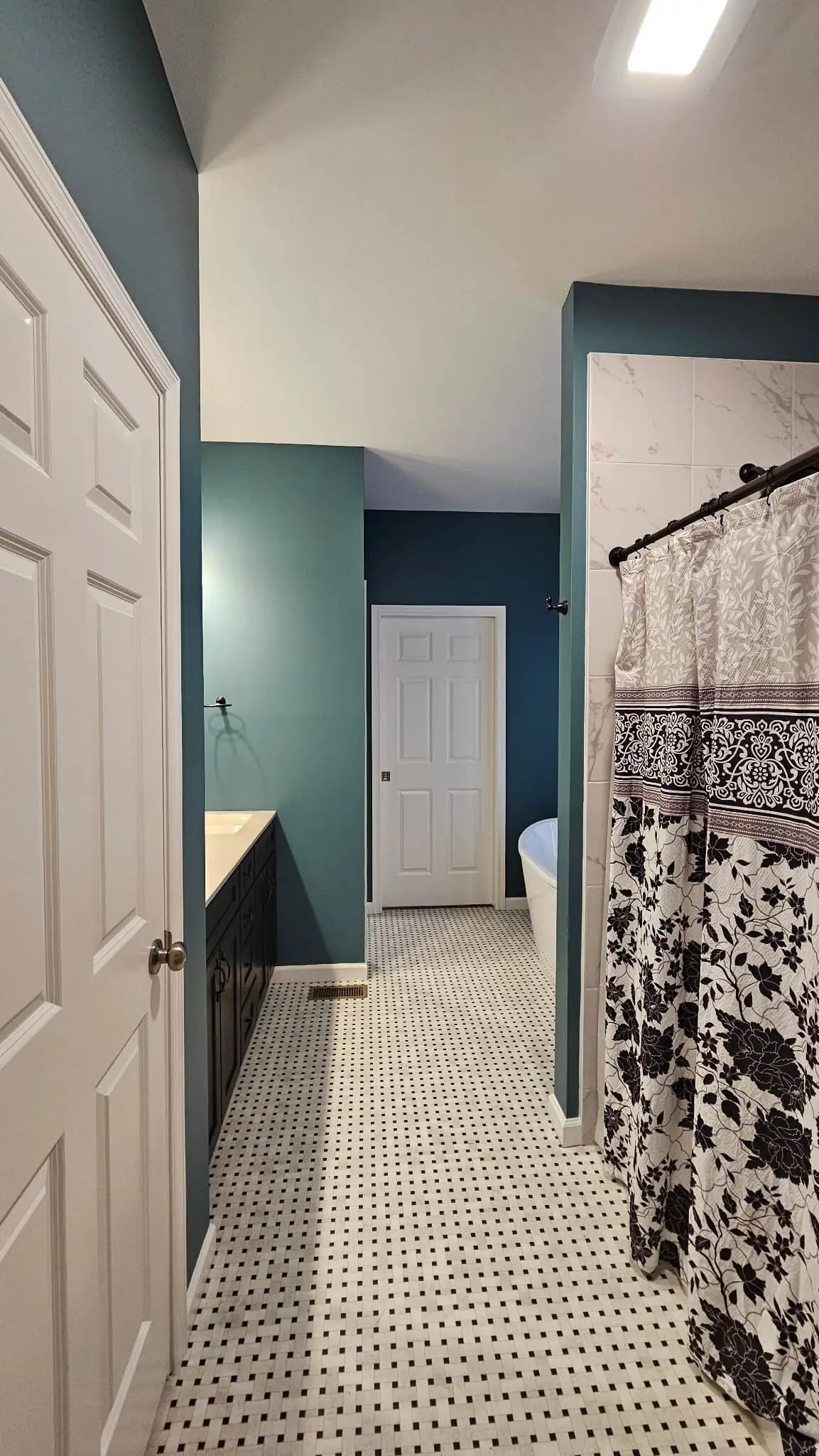 martzalls custom surface showcases a meticulously tidied bathroom with deep teal walls, classic mosaic floor tiling, and a stylish floral-patterned shower curtain.