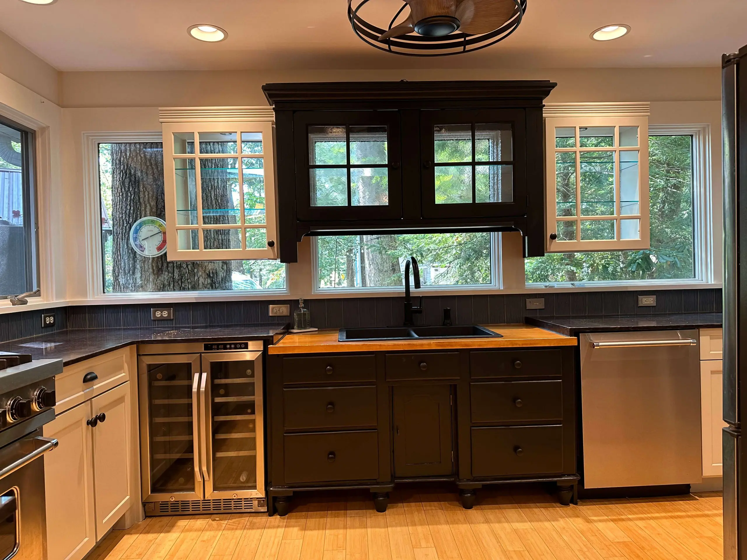 Modern kitchen remodel by Martzall's Custom Surfaces featuring black cabinetry, butcher block island, dual-zone wine cooler, and elegant glass-front cupboards.