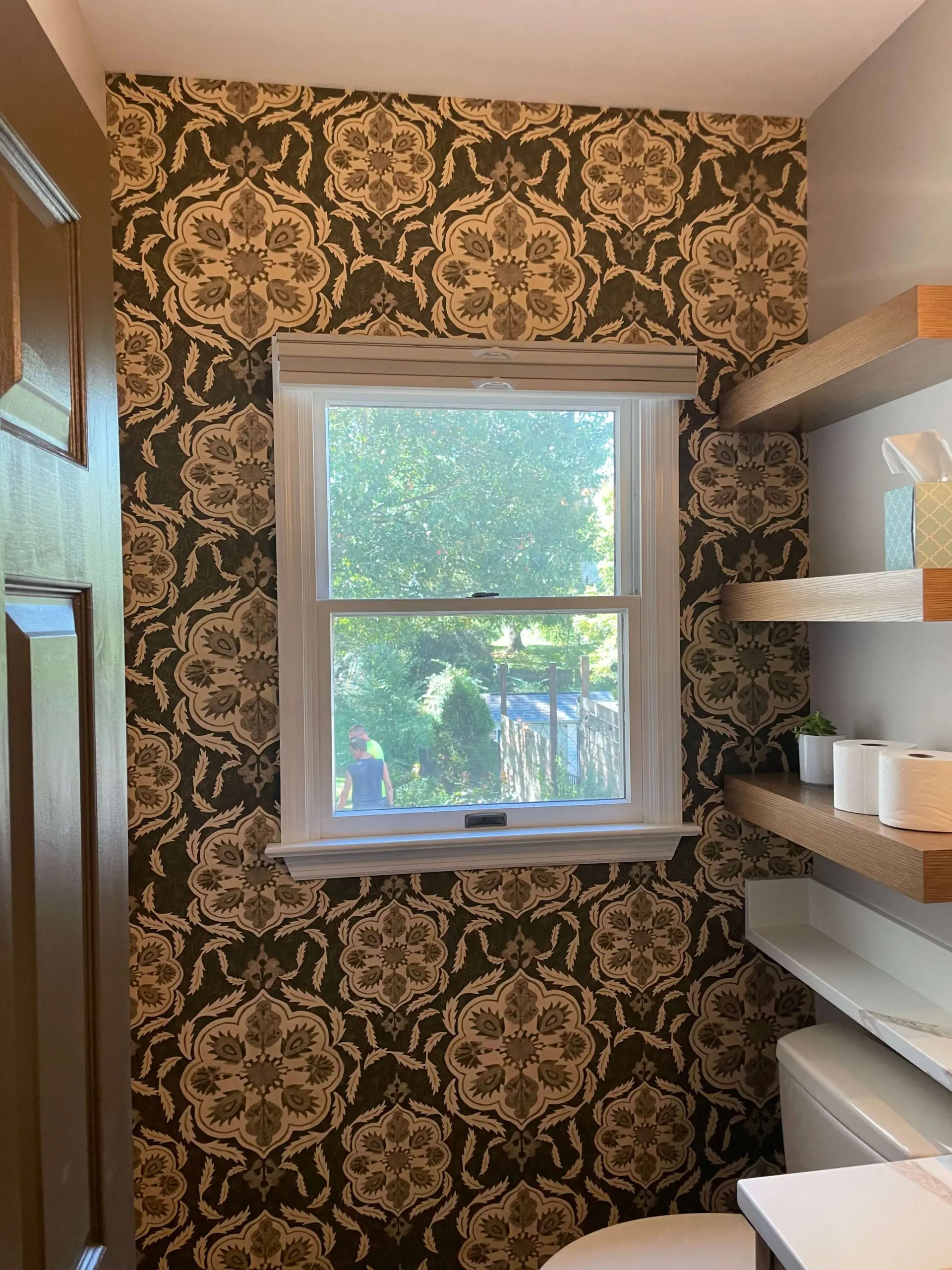 Bathroom accent wall featuring ornate damask wallpaper and floating wood shelves installed by Martzall's Custom Surfaces.