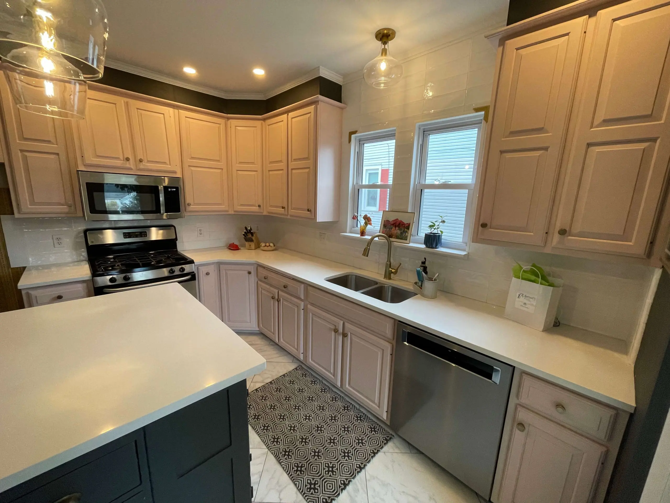 Modern kitchen remodel showcases Martzall's Custom Surfaces sleek white quartz countertops paired with blush-toned cabinets and a dark contrast island.