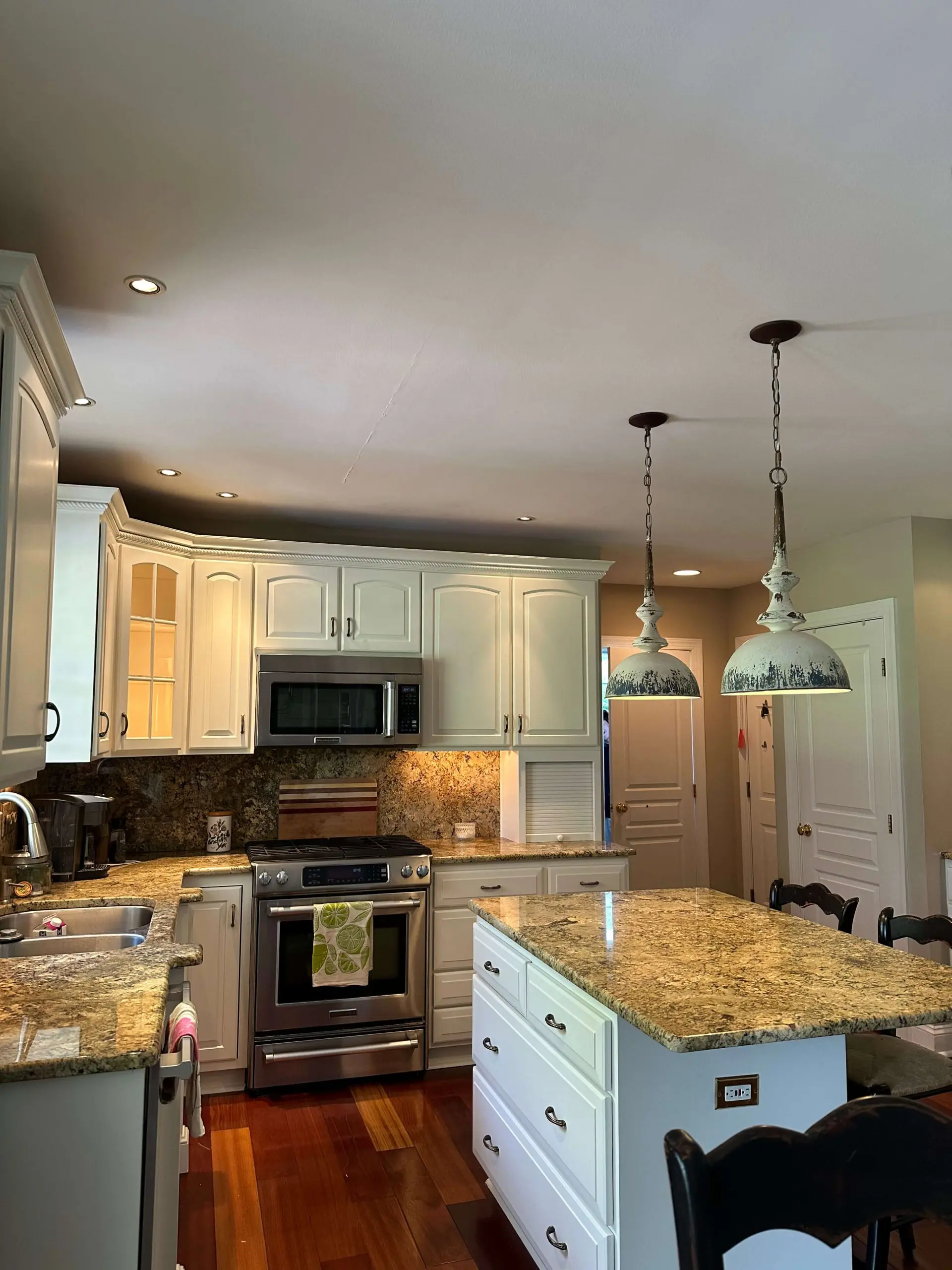Elegant kitchen island and matching backsplash by Martzall's Custom Surfaces featuring Earth-toned granite, stainless appliances, and vintage-style pendant lamps.