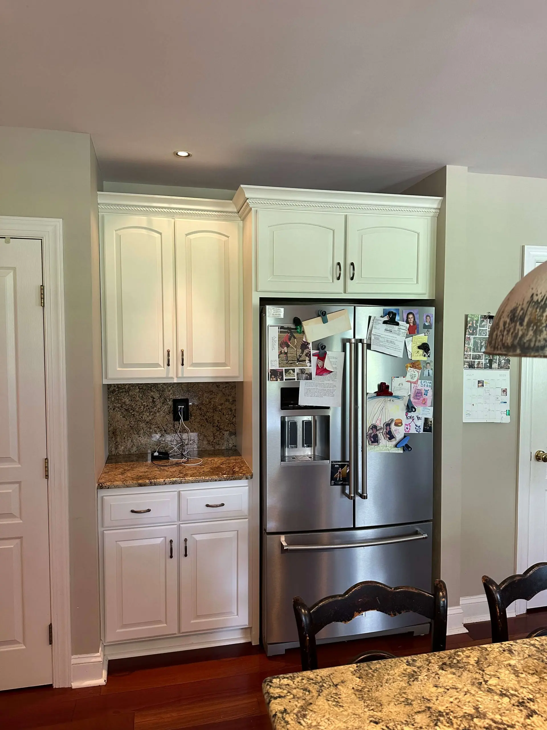White kitchen remodel with custom granite countertops by Martzall's Custom Surfaces featuring a matching backsplash and built-in refrigerator alcove.