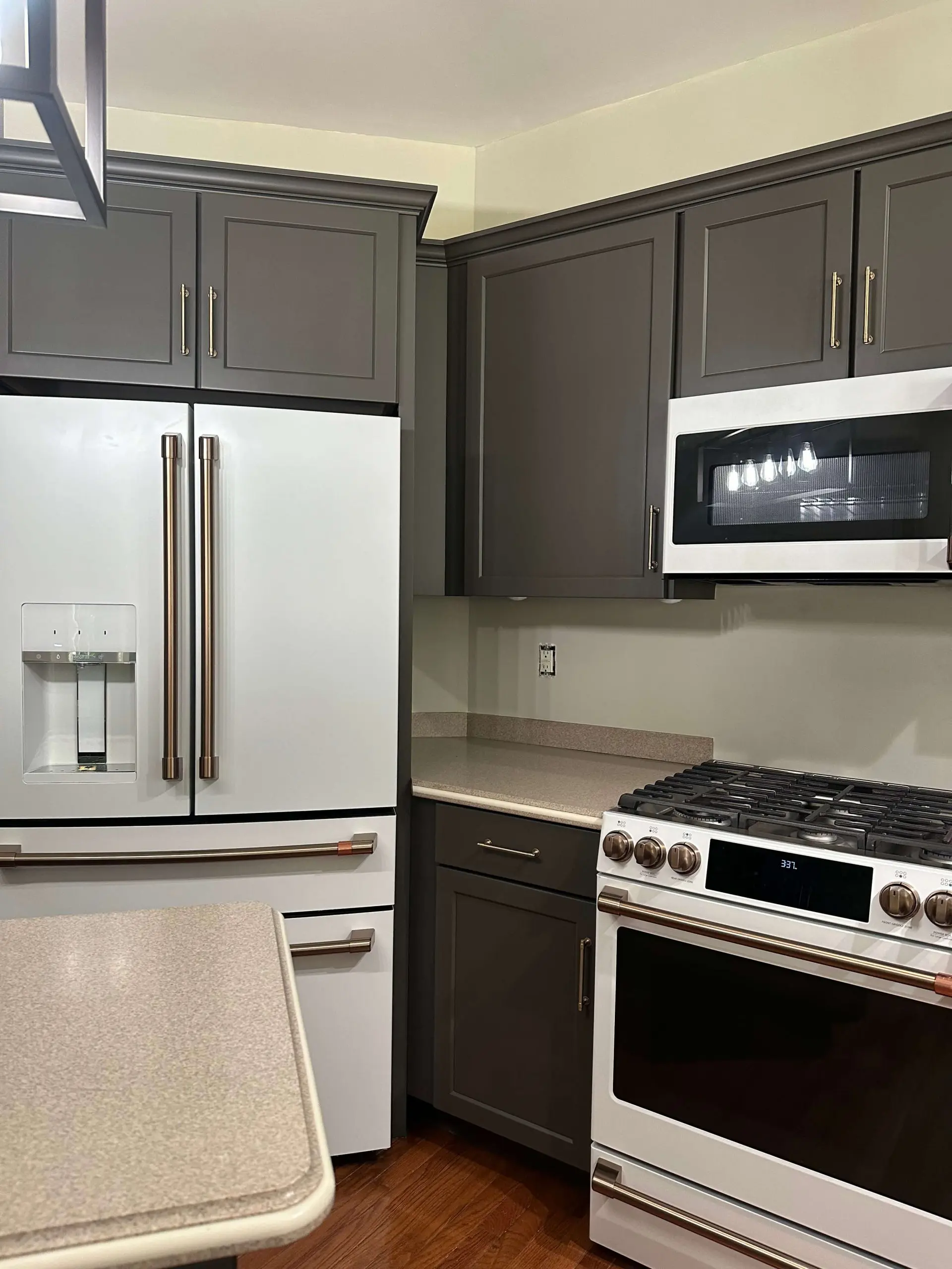Dark gray kitchen cabinets contrast with matte white appliances featuring bronze handles, impeccably sanitized by martzalls custom surface. for a spotless finish.