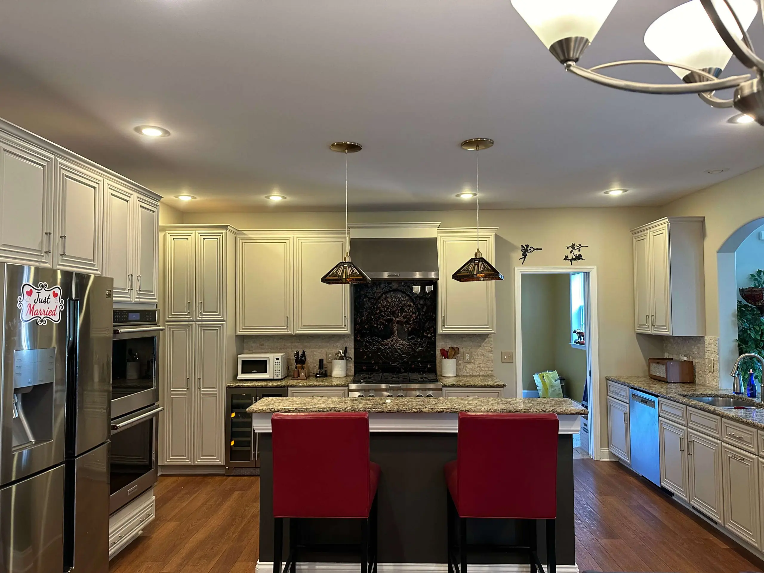 Modern kitchen renovation by Martzall's Custom Surfaces featuring a granite island, stainless appliances, red barstools, and a decorative tree backsplash.