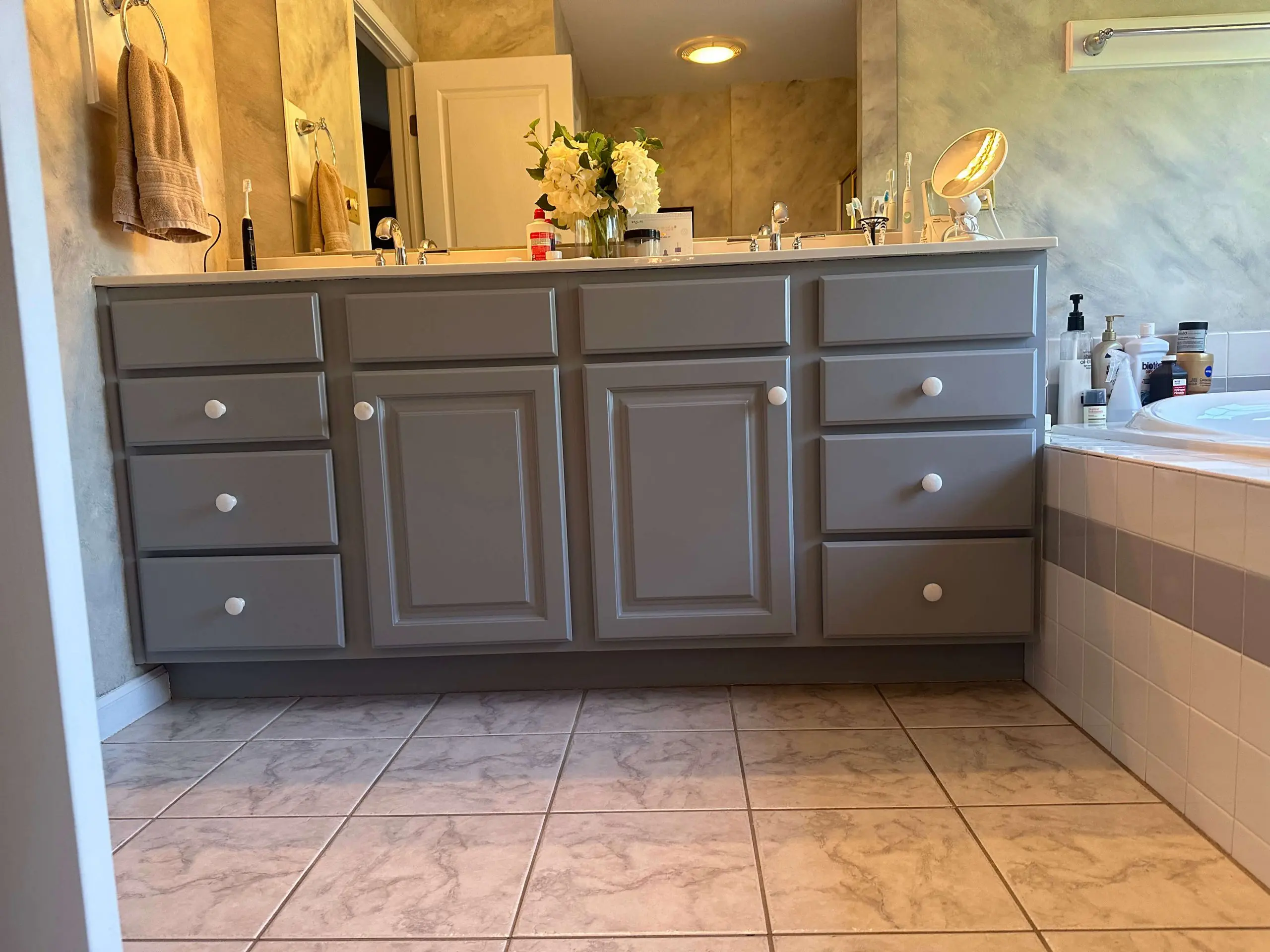 Modern gray bathroom vanity with white knobs and marble tile flooring, professionally detailed by martzalls custom surface.