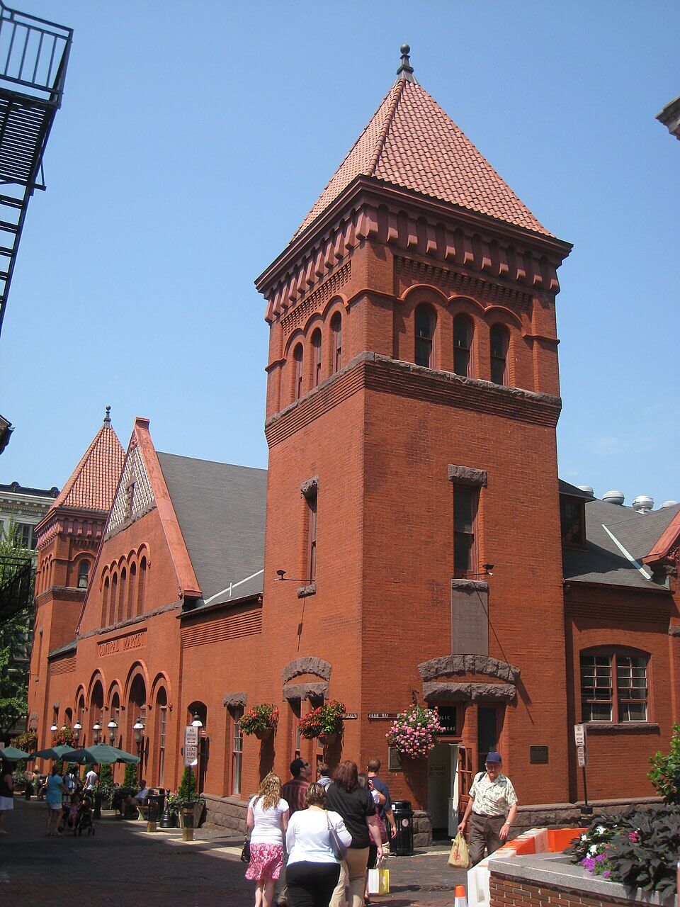 Historic red brick market building with a towering steeple, enjoyed by shoppers and maintained.