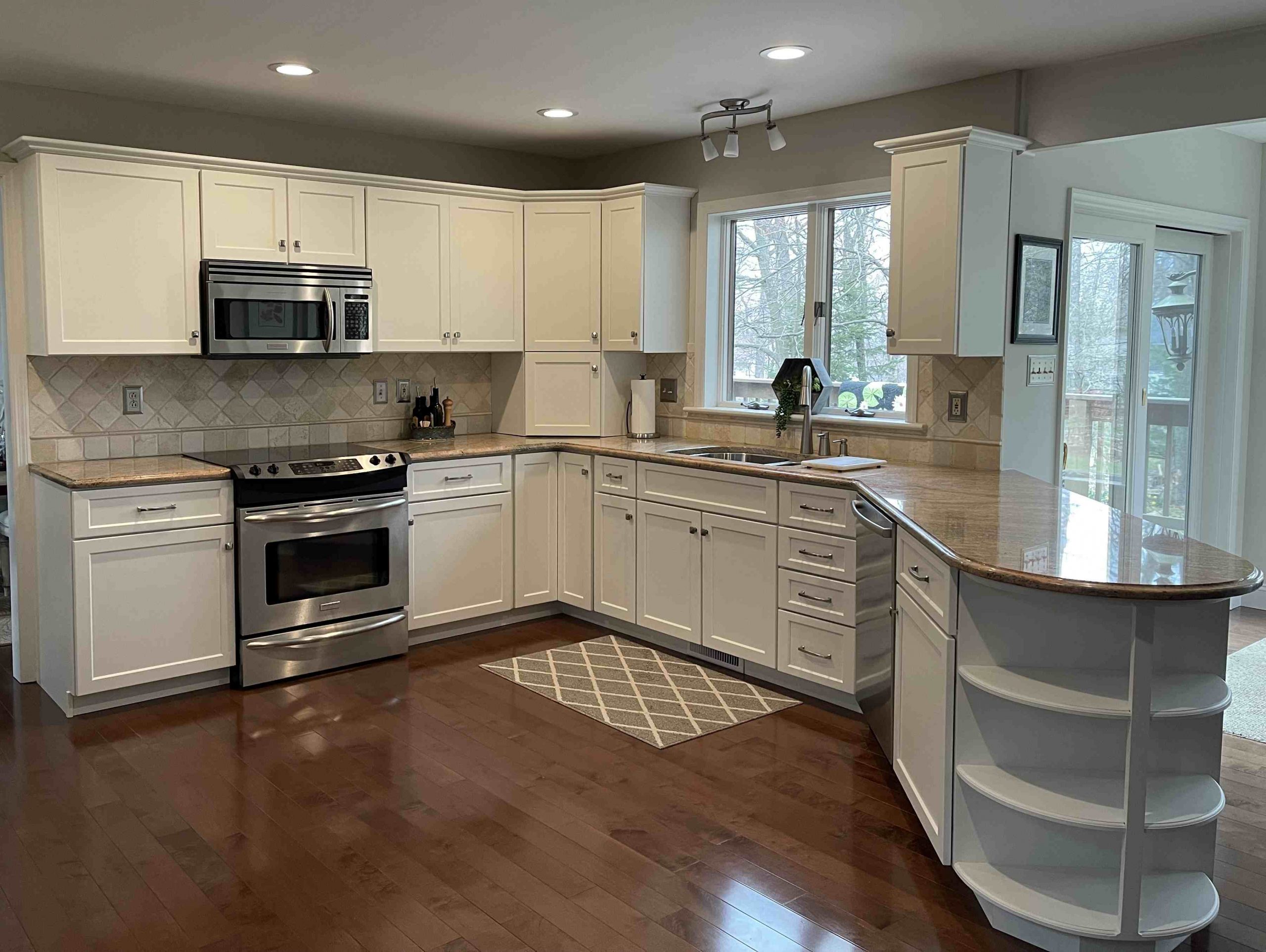 A bright, modern kitchen by Penguin Clean Co featuring white cabinets, stainless steel appliances, and polished granite countertops on a dark hardwood floor.