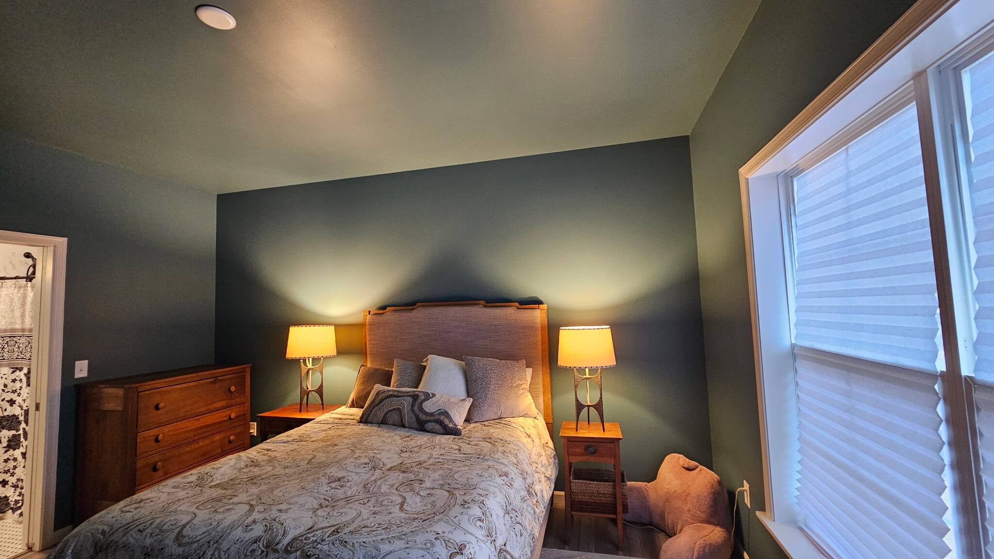 Cozy bedroom with deep blue accent wall, warm bedside lighting, wood furniture, and crisp white trim creating a calm and inviting retreat space
