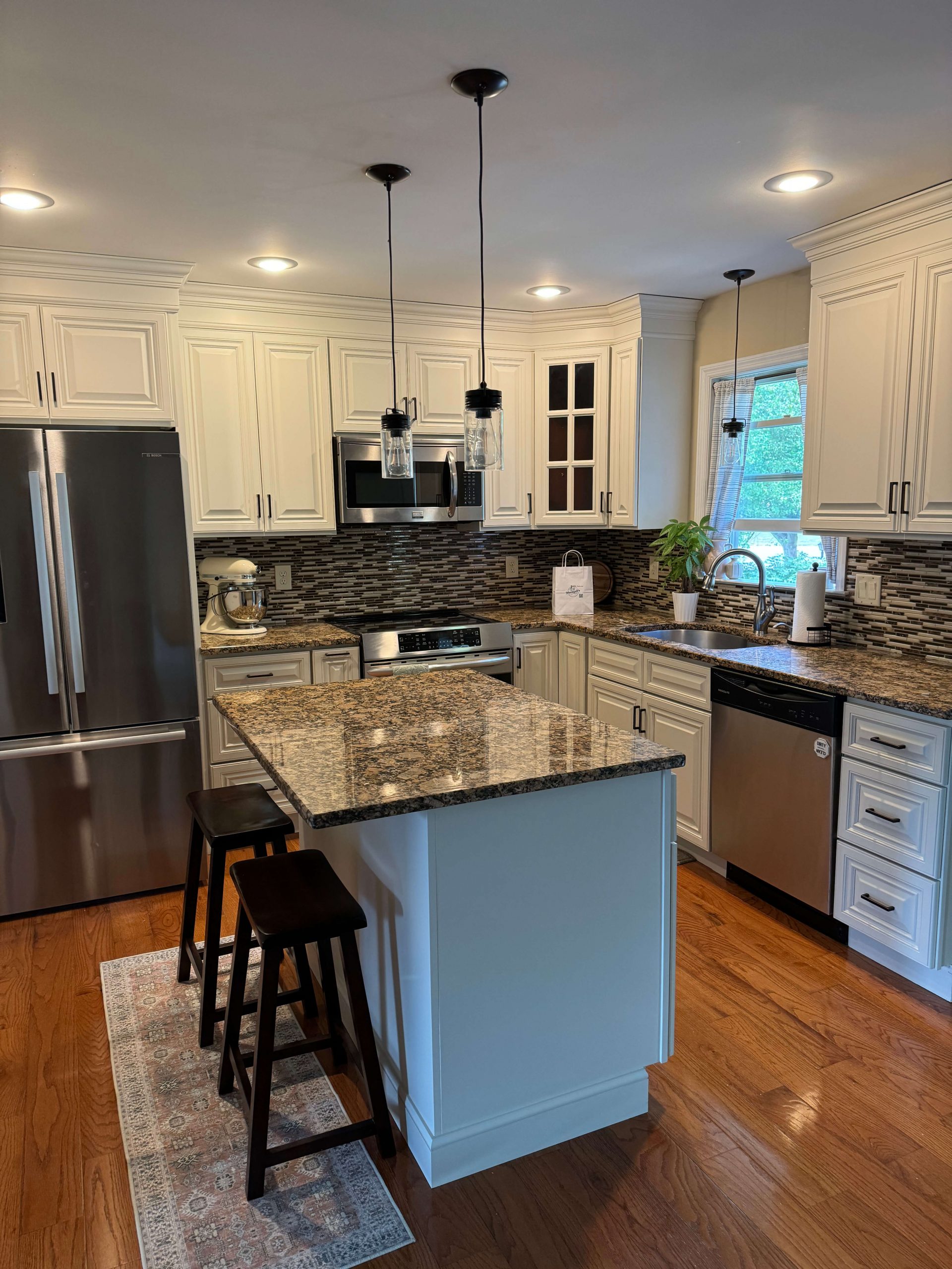 Martzall's Custom Surfaces features a luxury kitchen remodel with brown granite countertops, white cabinetry, a mosaic tile backsplash, and stainless steel appliances over rich oak floors.