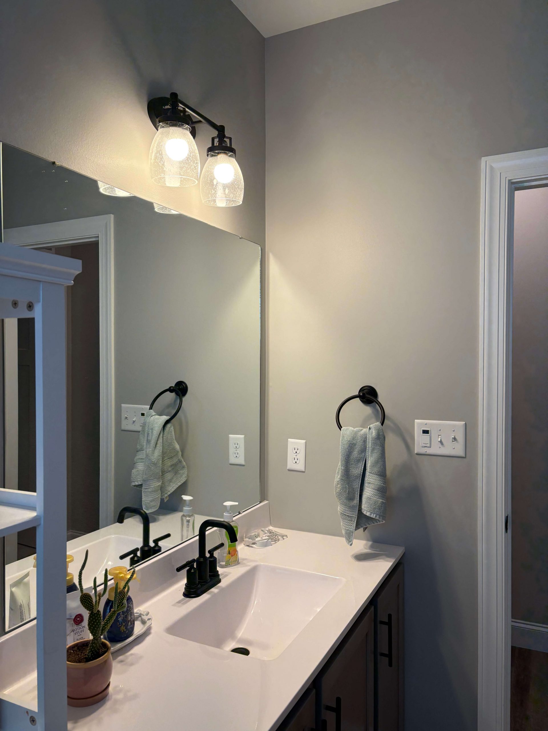 Martzall's Custom Surfaces contemporary bathroom renovation showcasing a sleek white vanity, matte black fixtures, and soft grey walls under warm globe lighting.