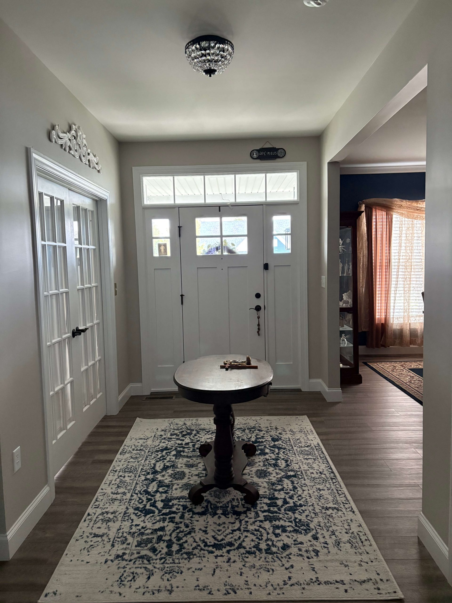 Inviting home entryway showcasing premium wide-plank flooring by Martzall's Custom Surfaces, complemented by a classic white craftsman door, French doors, and a decorative blue area rug.
