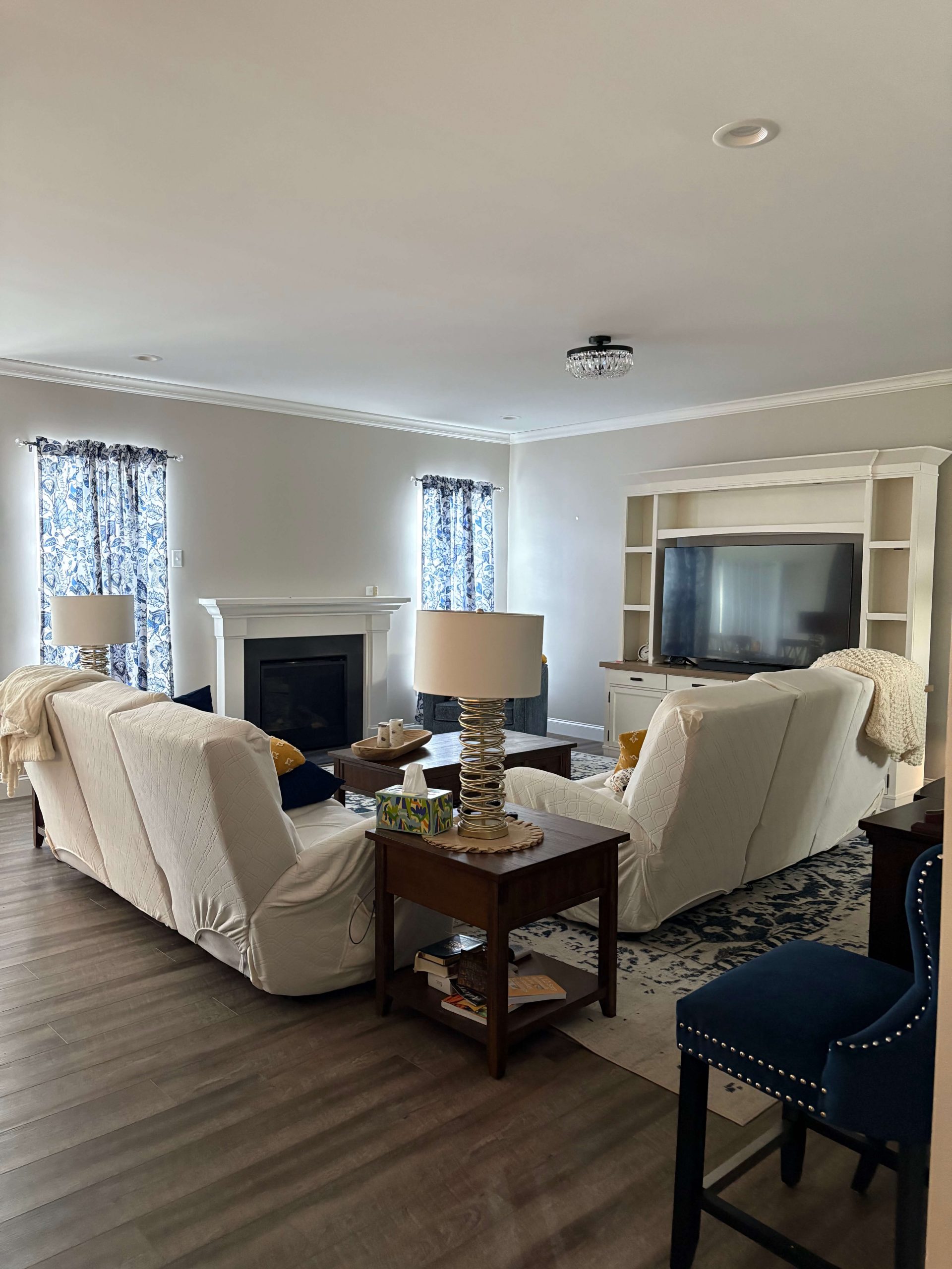 Spacious living room featuring elegant wood flooring and a classic white fireplace mantel installed by Martzall's Custom Surfaces, accented by blue patterned curtains and neutral sofas.