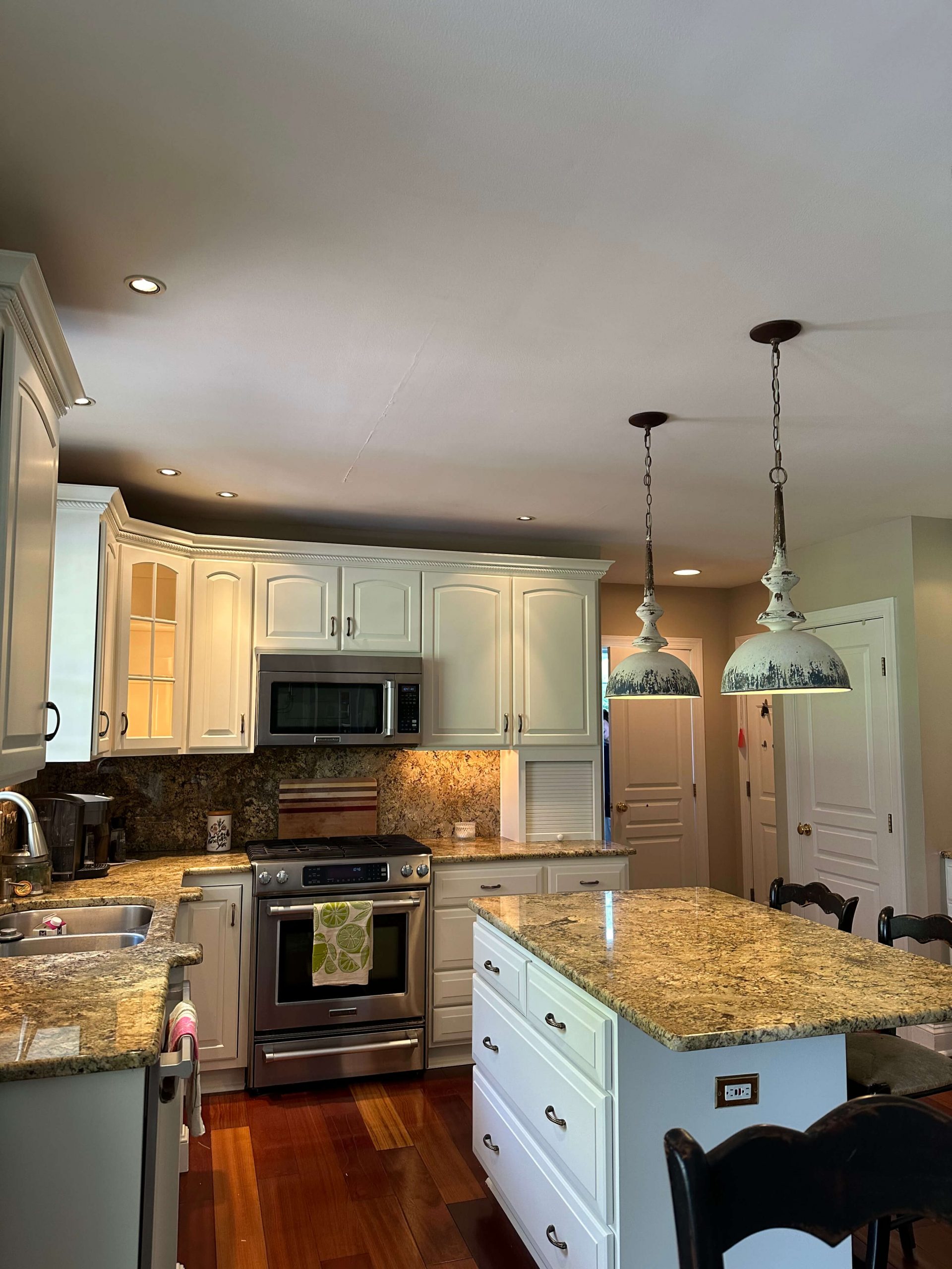Elegant kitchen island and matching backsplash by Martzall's Custom Surfaces featuring Earth-toned granite, stainless appliances, and vintage-style pendant lamps.