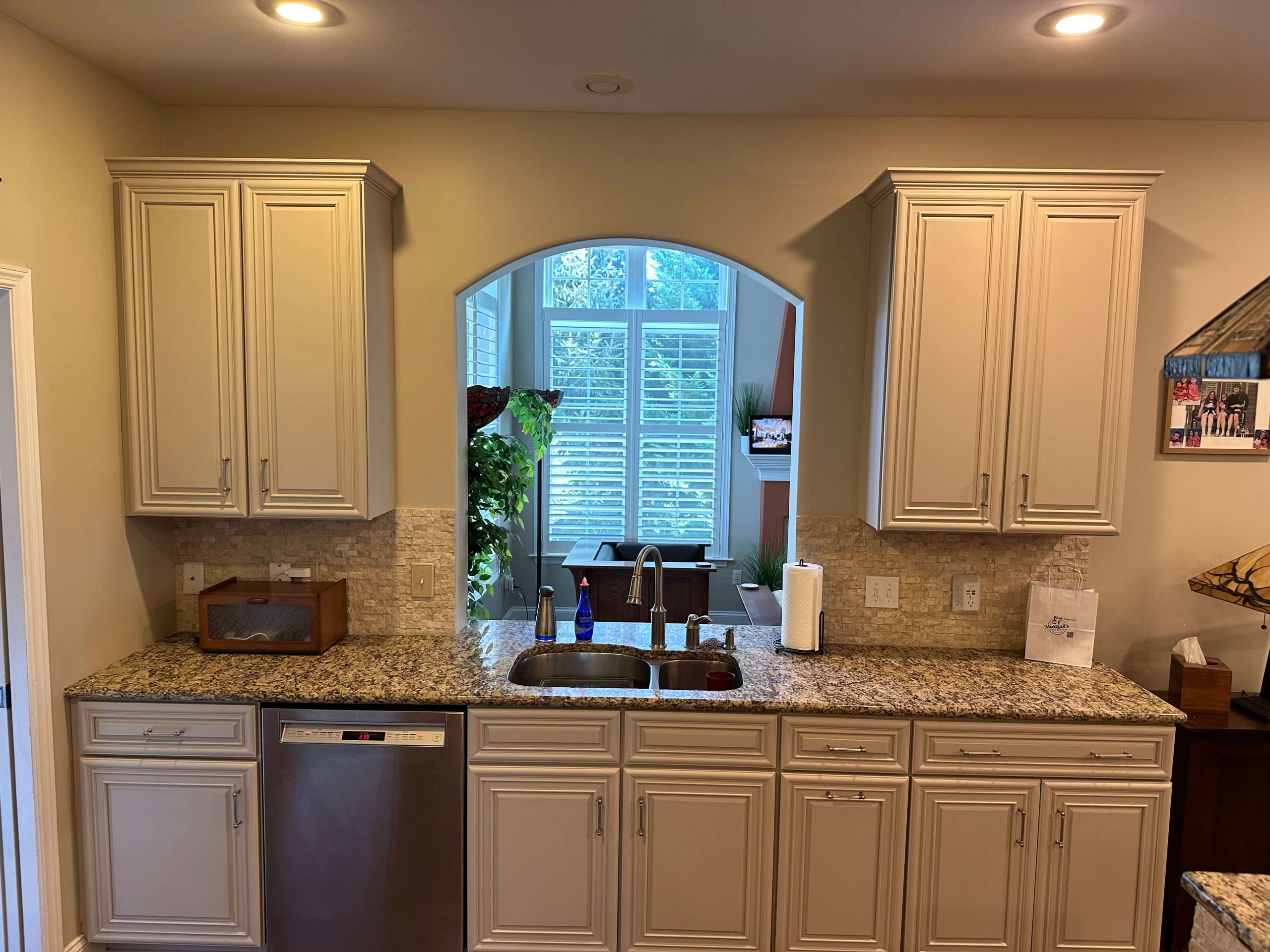 Custom kitchen remodel featuring neutral cabinets and granite countertops by Martzall's Custom Surfaces with a view through an arched pass-through window.