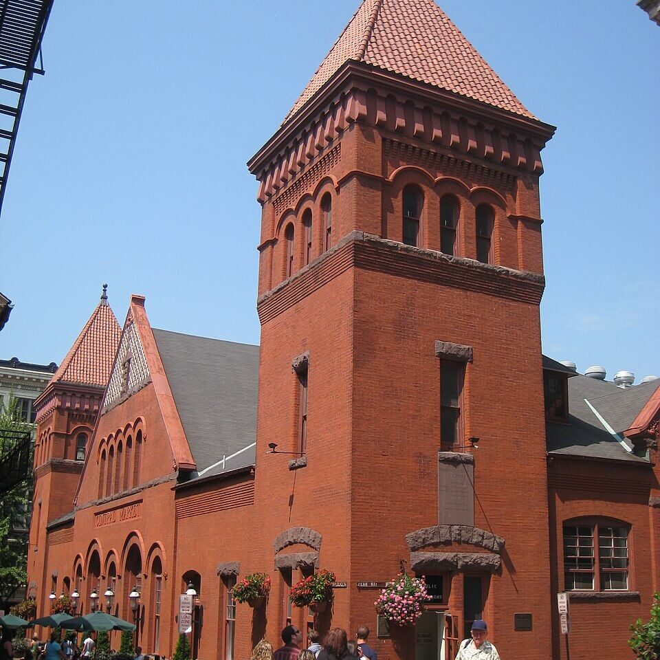 Historic red brick market building with a towering steeple, enjoyed by shoppers and maintained.
