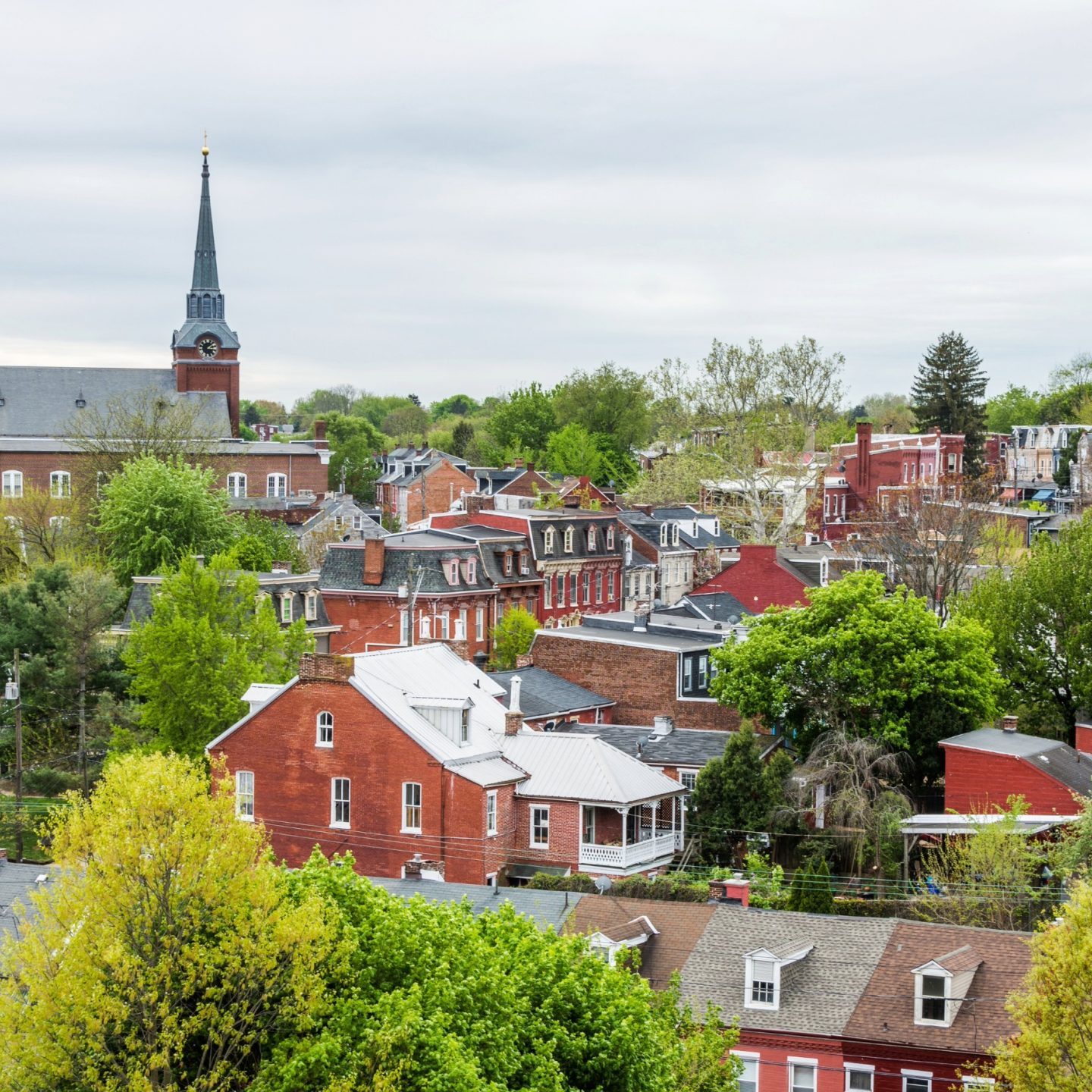 Scenic aerial view of a historic brick town neighborhood featuring lush green trees and a prominent church steeple, serviced by Penguin Clean Co.