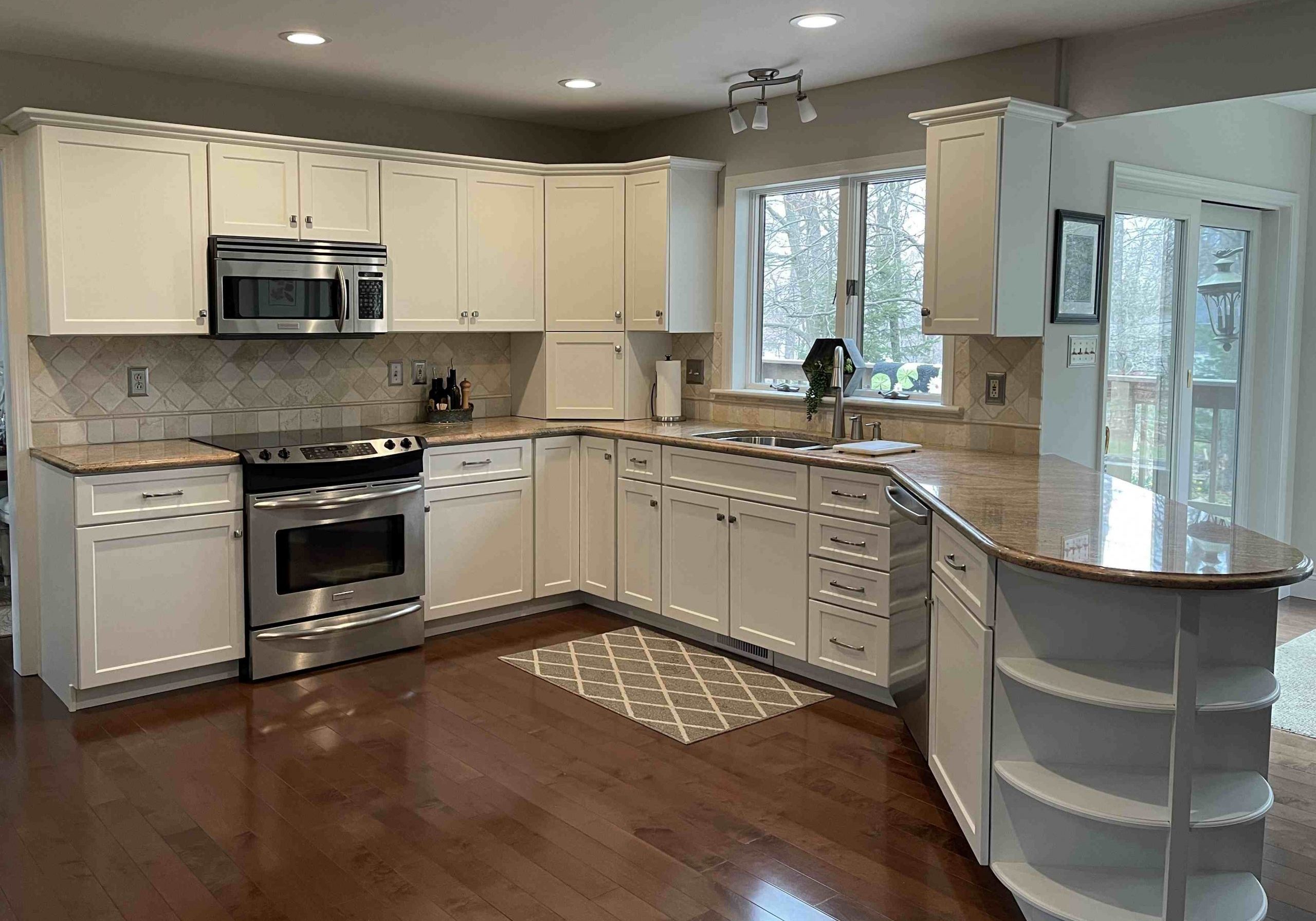 A bright, modern kitchen by Penguin Clean Co featuring white cabinets, stainless steel appliances, and polished granite countertops on a dark hardwood floor.