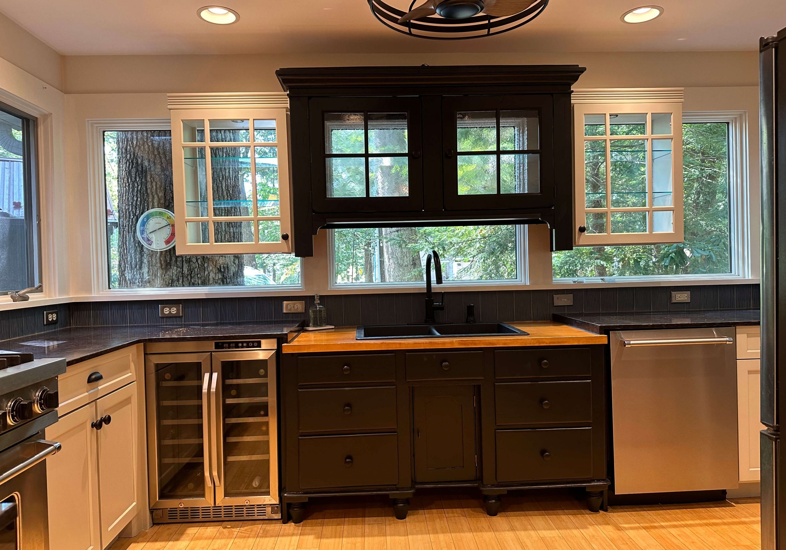 Modern kitchen remodel by Martzall's Custom Surfaces featuring black cabinetry, butcher block island, dual-zone wine cooler, and elegant glass-front cupboards.