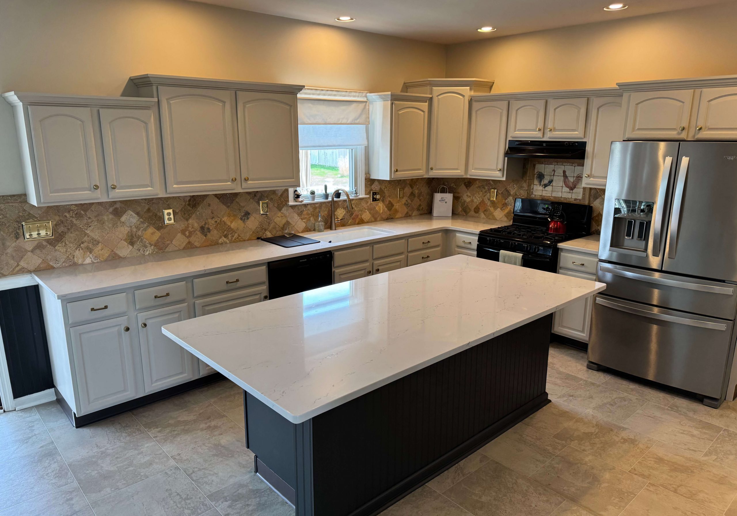 A bright kitchen featuring elegant white marble countertops and a dark gray island installed by Martzall's Custom Surfaces.